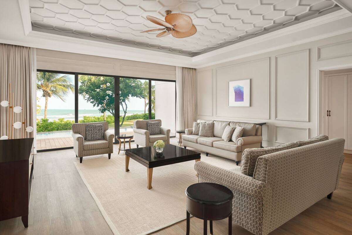 Een ruime woonkamer met een groot raam dat uitzicht biedt op de oceaan, een plafondventilator en een modern interieur.