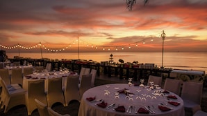 Een terras met ronde tafels klaar voor een maaltijd, met uitzicht op een wateroppervlak tijdens de zonsondergang.