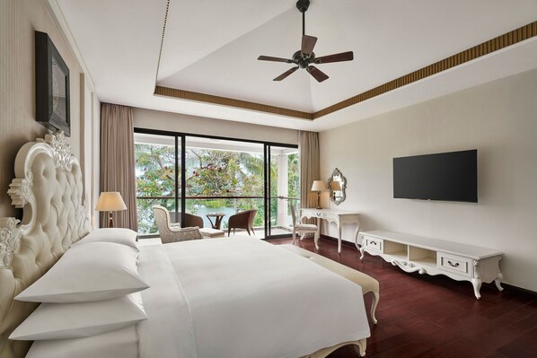 Un dormitorio espacioso con una cama grande, ventilador de techo, televisión y balcón con vistas a árboles.