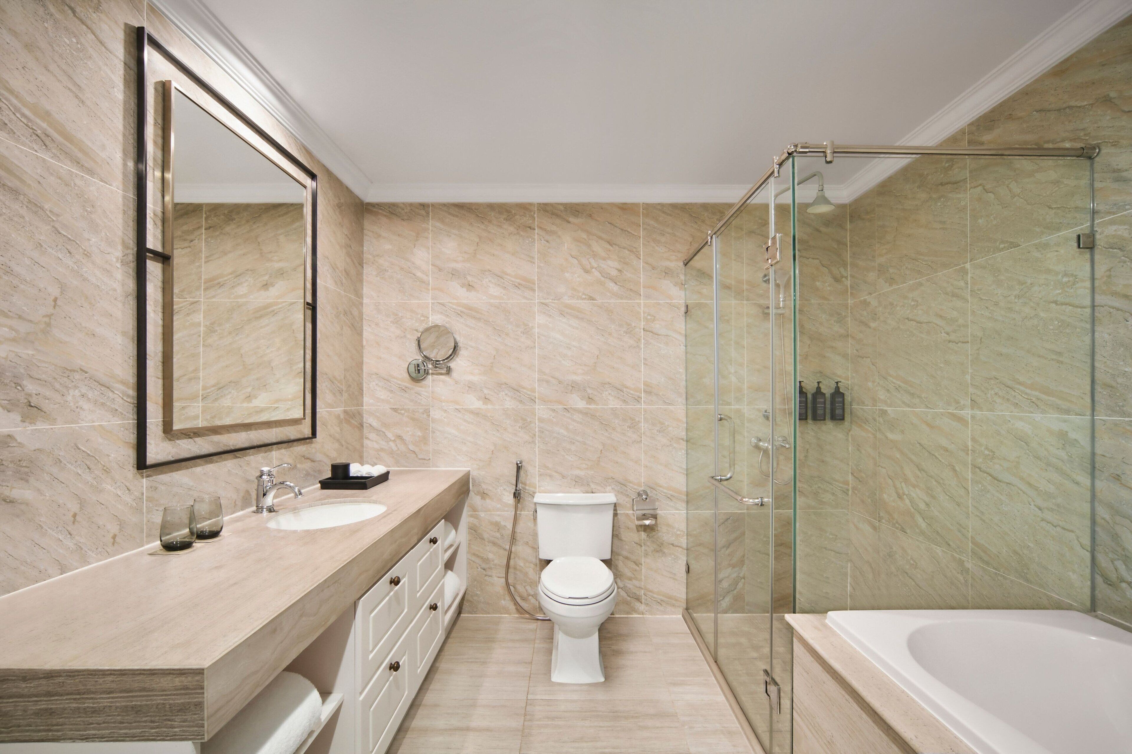 Une salle de bain moderne avec un sol en marbre, une douche à parois de verre, des toilettes blanches et une grande baignoire.