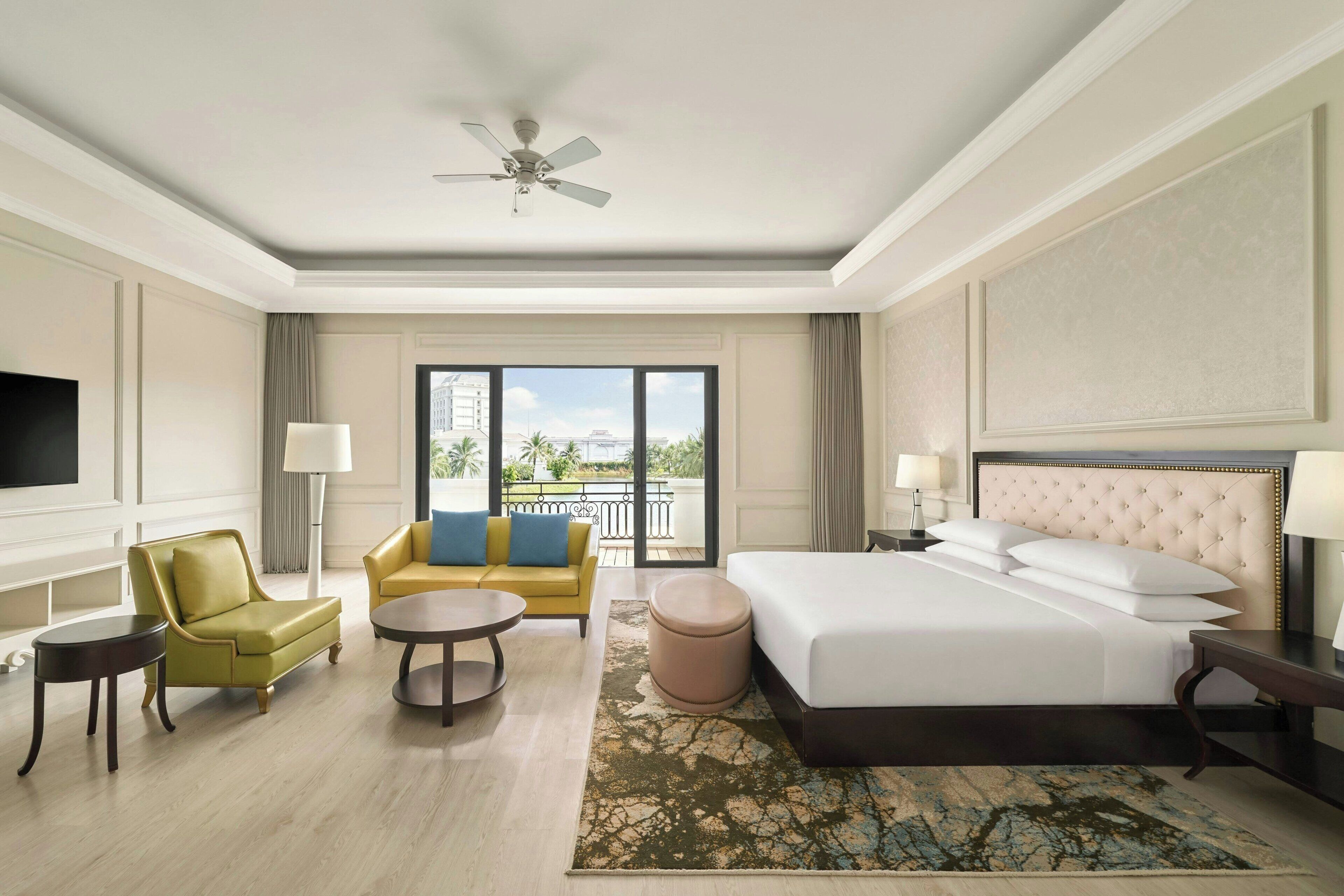 Una habitación de hotel con cama, sofá, sillón, mesita y ventilador de techo.