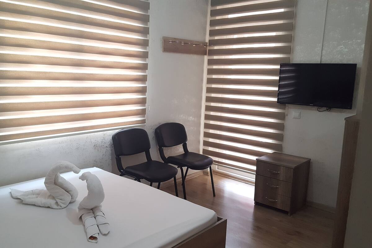 Una habitación de hotel con cama, dos sillones, televisor y aparador de madera.