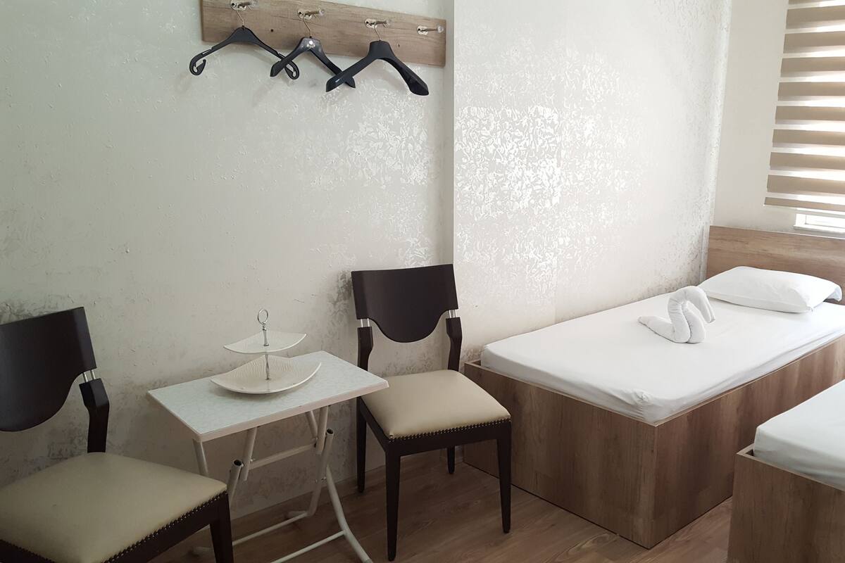 Habitación de hotel compacta con una cama individual, una mesita pequeña, dos sillas y un perchero en la pared.