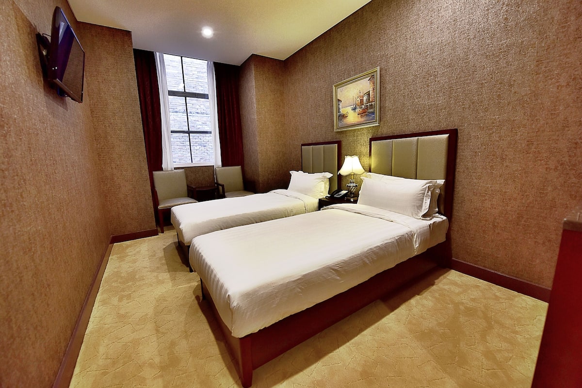 A hotel room with two beds, a TV, a painting, and a window.