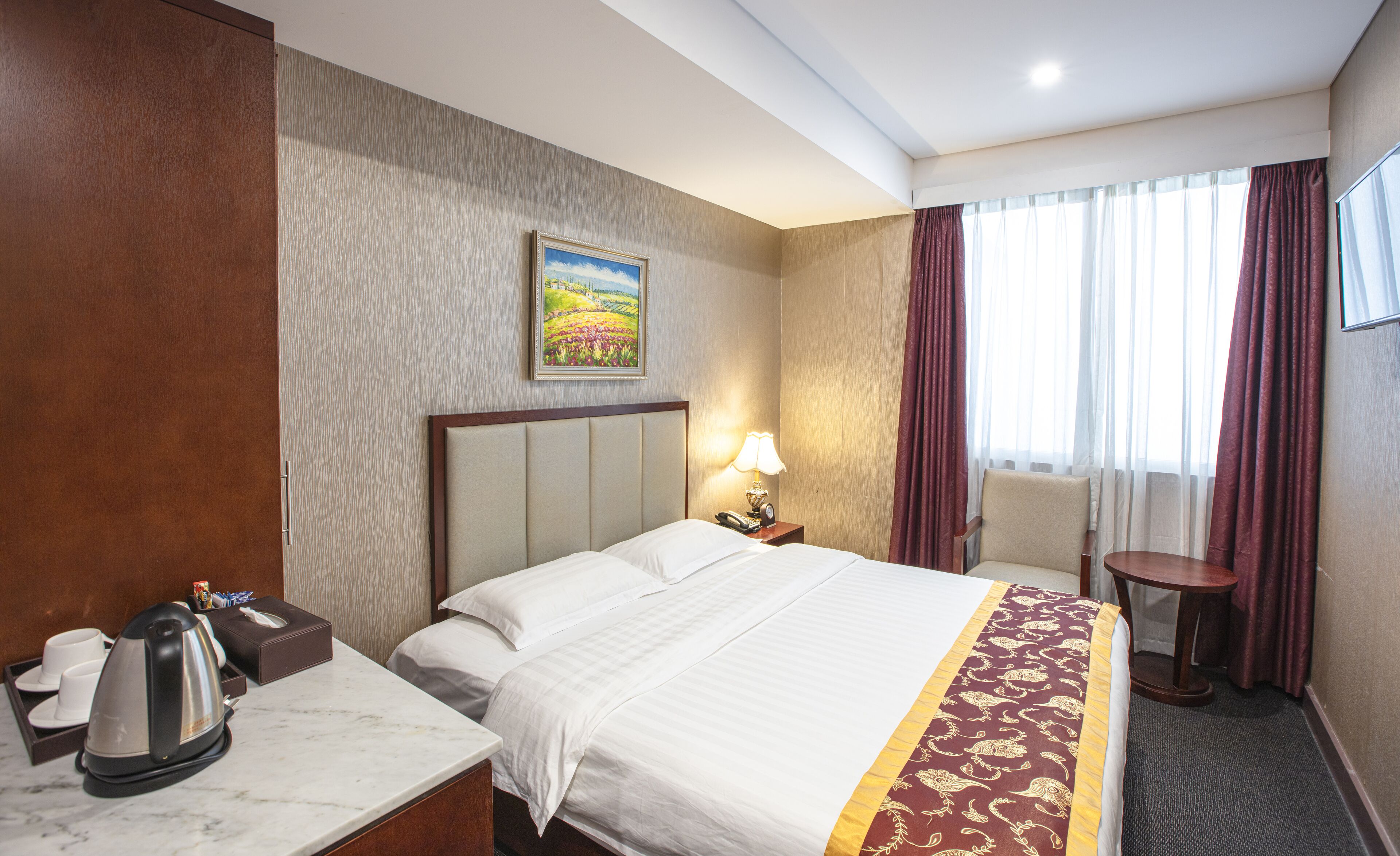 A hotel room with a bed, bedside table, lamp, and a painting on the wall.