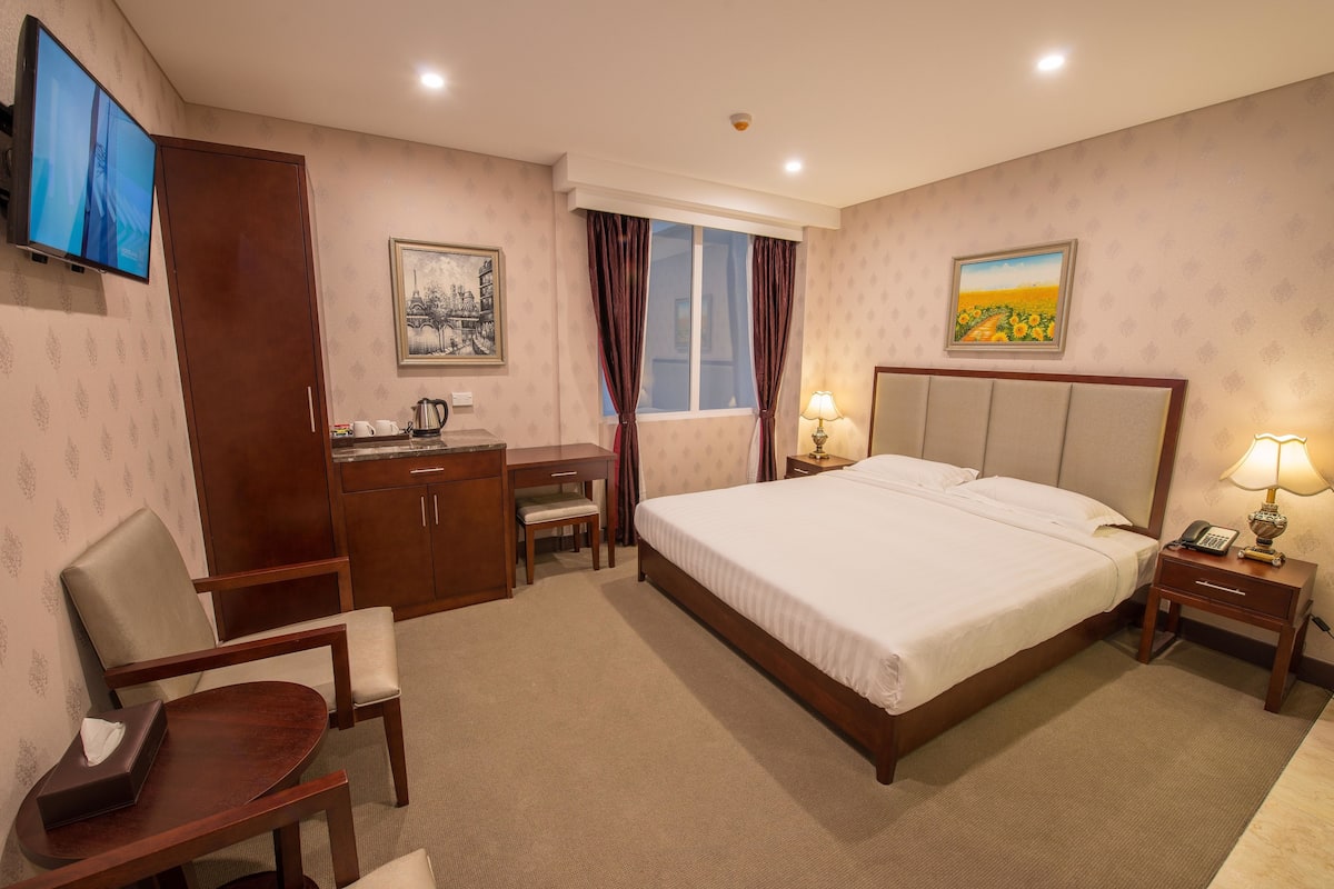 A hotel room with a bed, desk, chair, and a television.