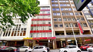 A street view with cars parked in front of a building with multiple shops, including a visible sign for 'Sign of the Times'. - Megaboom City Hotel (Sydney)