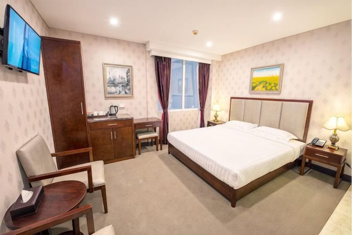 A hotel room with a bed, desk, chair, TV, and artwork on the walls.