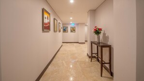 A hallway with a marble floor, framed artwork on the walls, and a small table with a vase of flowers. - Megaboom City Hotel (Sydney)