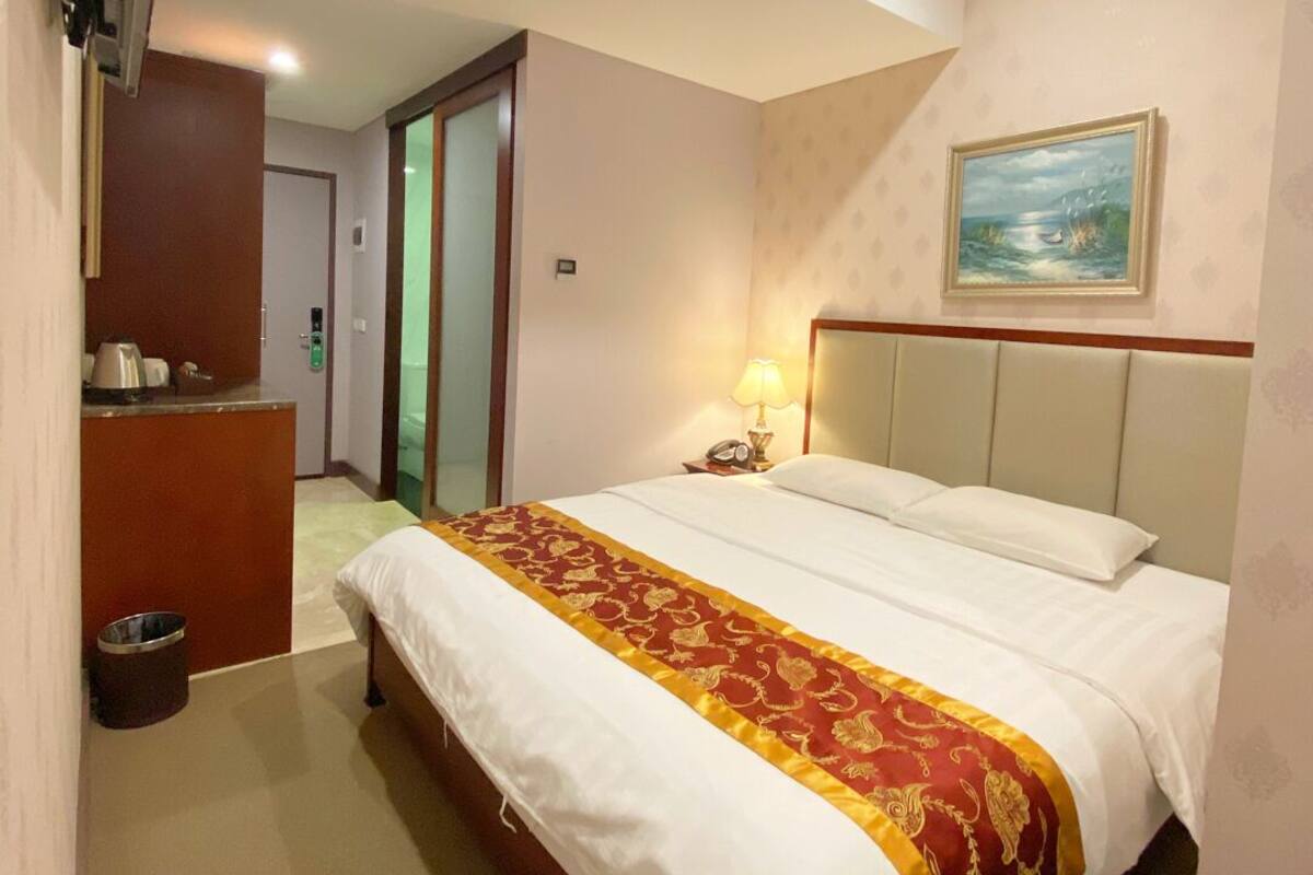 A hotel room with a bed, a desk, a chair, a TV mounted on the wall, and a painting on the wall.