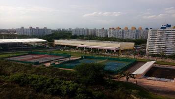 A sports complex with multiple tennis courts, a covered seating area, and a large building in the background.