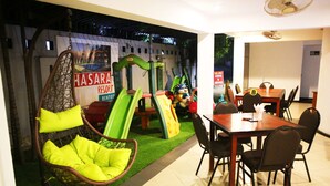 A dining area with a table and chairs, a hanging chair with cushions, and a children's play area with slides and toys. - Hasara Guest House (Galle)