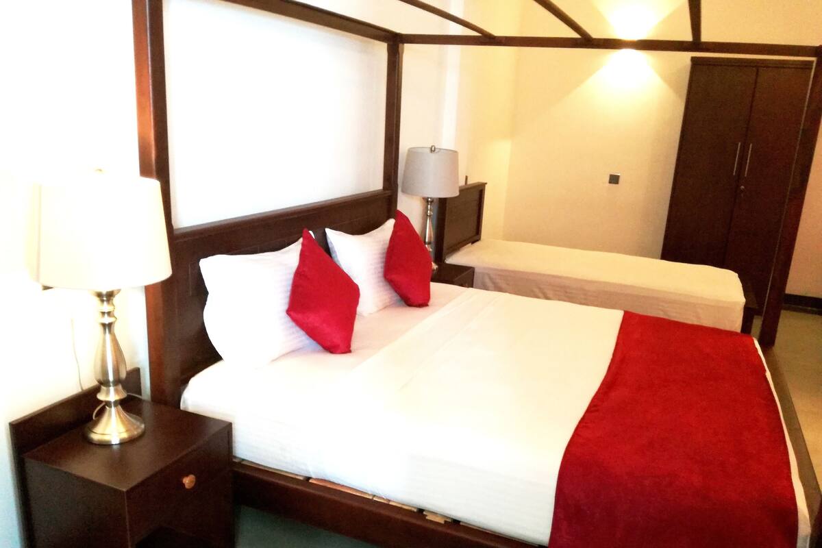 A hotel room with a large bed, a bedside table with a lamp, a nightstand, and a wardrobe.