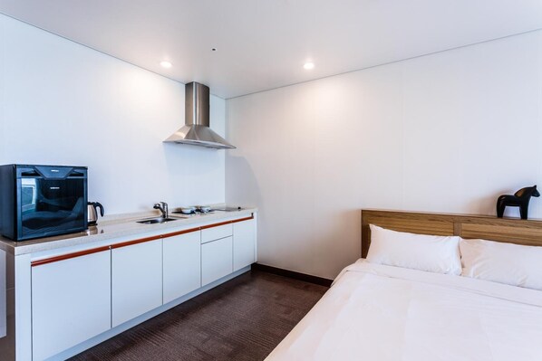 A modern hotel room with a kitchenette, a bed, and a mounted television. - Seastay Hotel & Spa (Jeju City)