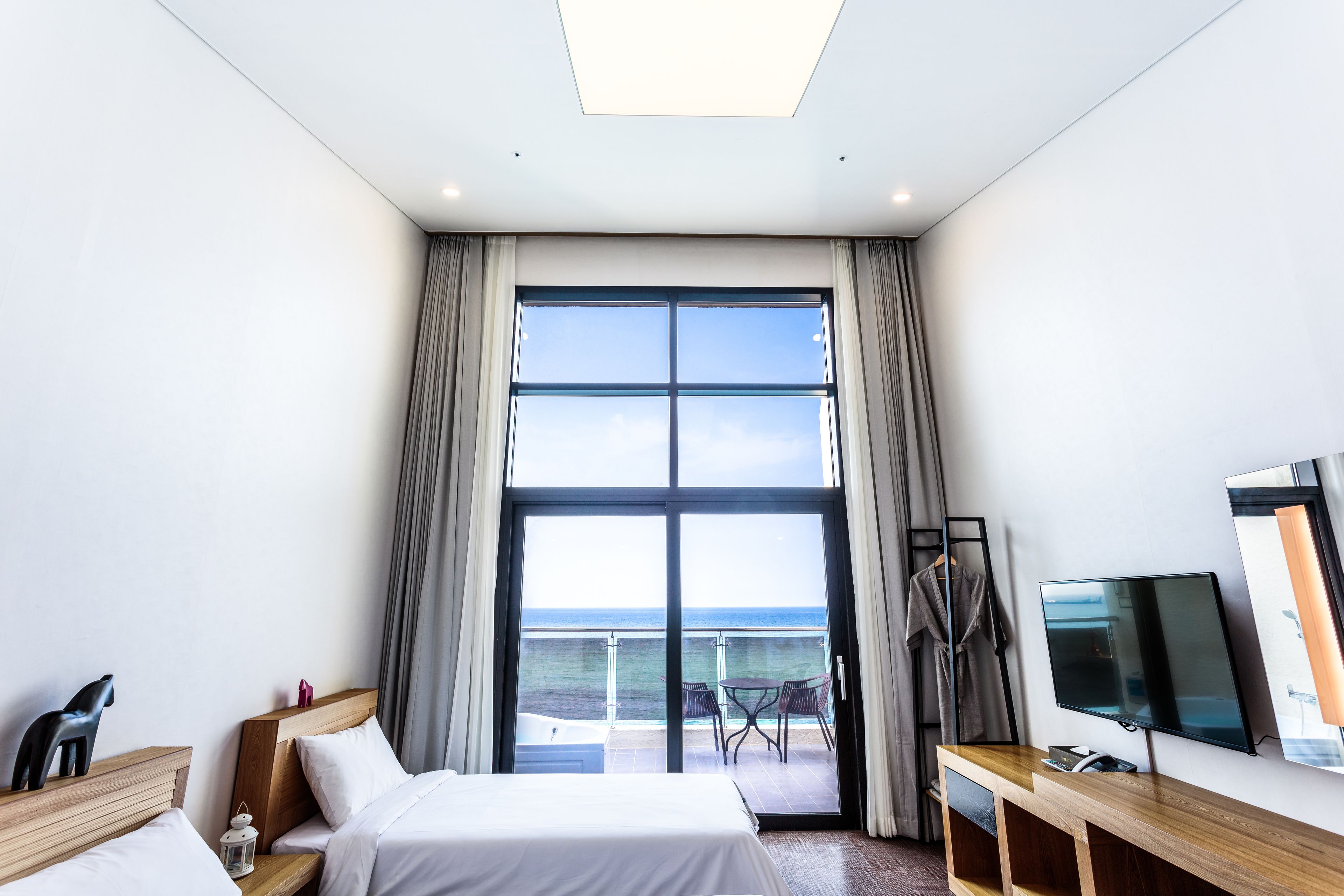 Quarto de hotel moderno com uma janela grande, uma cama, uma televisão e uma varanda com vista para o mar.