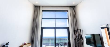 Quarto de hotel moderno com uma janela grande, uma cama, uma televisão e uma varanda com vista para o mar.