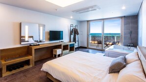 Een moderne hotelkamer met een groot bed, een bureau met een televisie, een douche en een balkon met uitzicht op de oceaan.