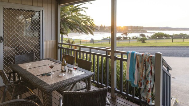 A covered outdoor seating area with a view of a body of water and a grassy area. - Reflections Bermagui - Holiday Park (Bermagui)