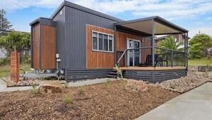 A modern house with a covered patio, a wooden deck, and a stone pathway. - Reflections Bermagui - Holiday Park (Bermagui)