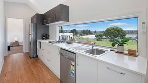 A modern kitchen with a large window, stainless steel appliances, and a view of a residential area. - Reflections Bermagui - Holiday Park (Bermagui)