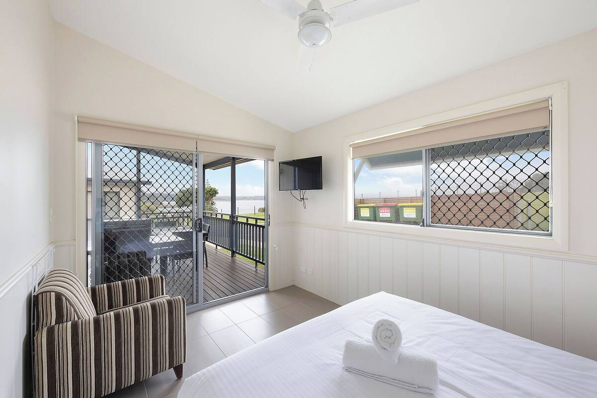 A bedroom with a bed, a TV, a balcony with a view, and a window with a screen.