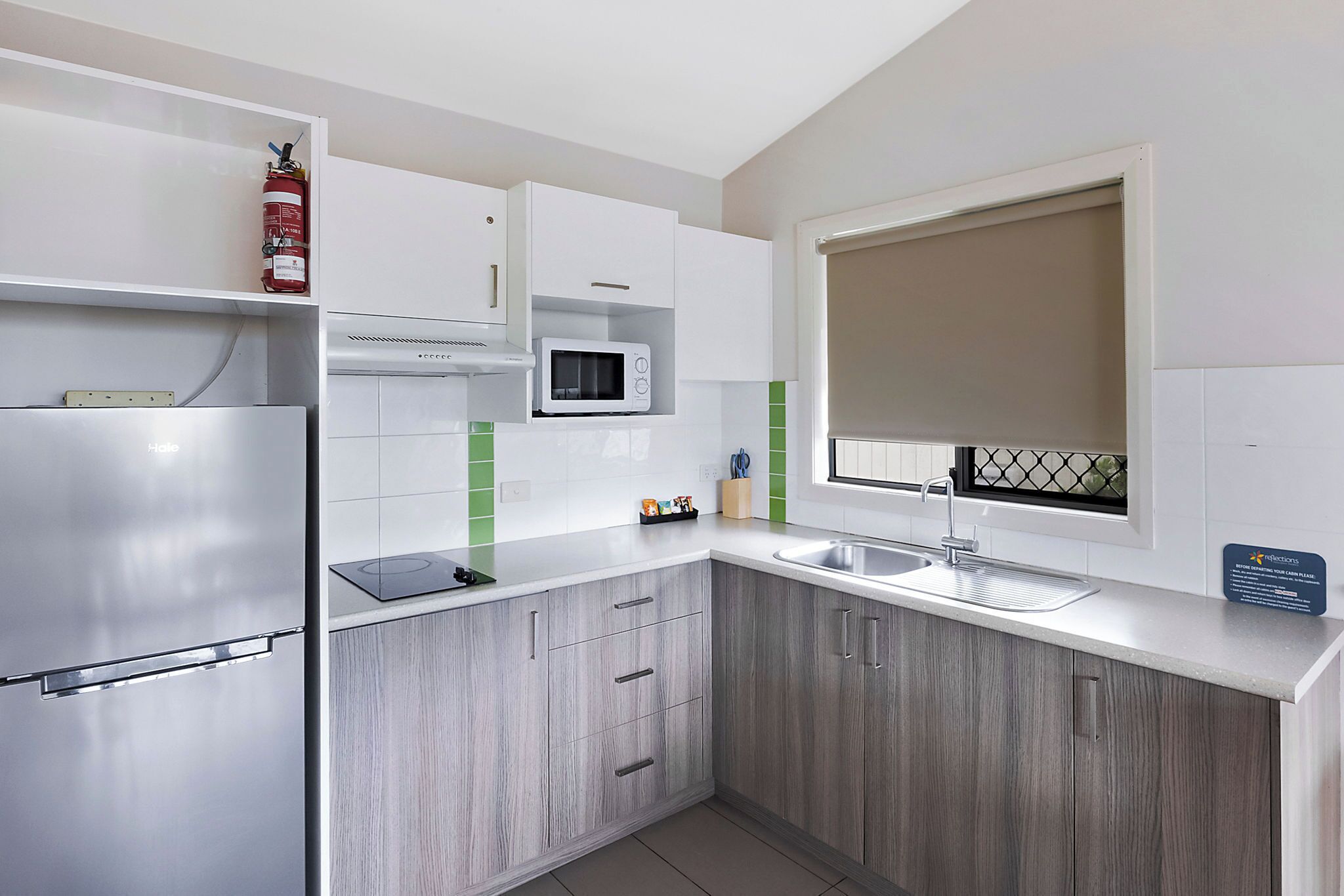 A modern kitchen with a stainless steel refrigerator, white cabinets, a microwave, and a window with a view.