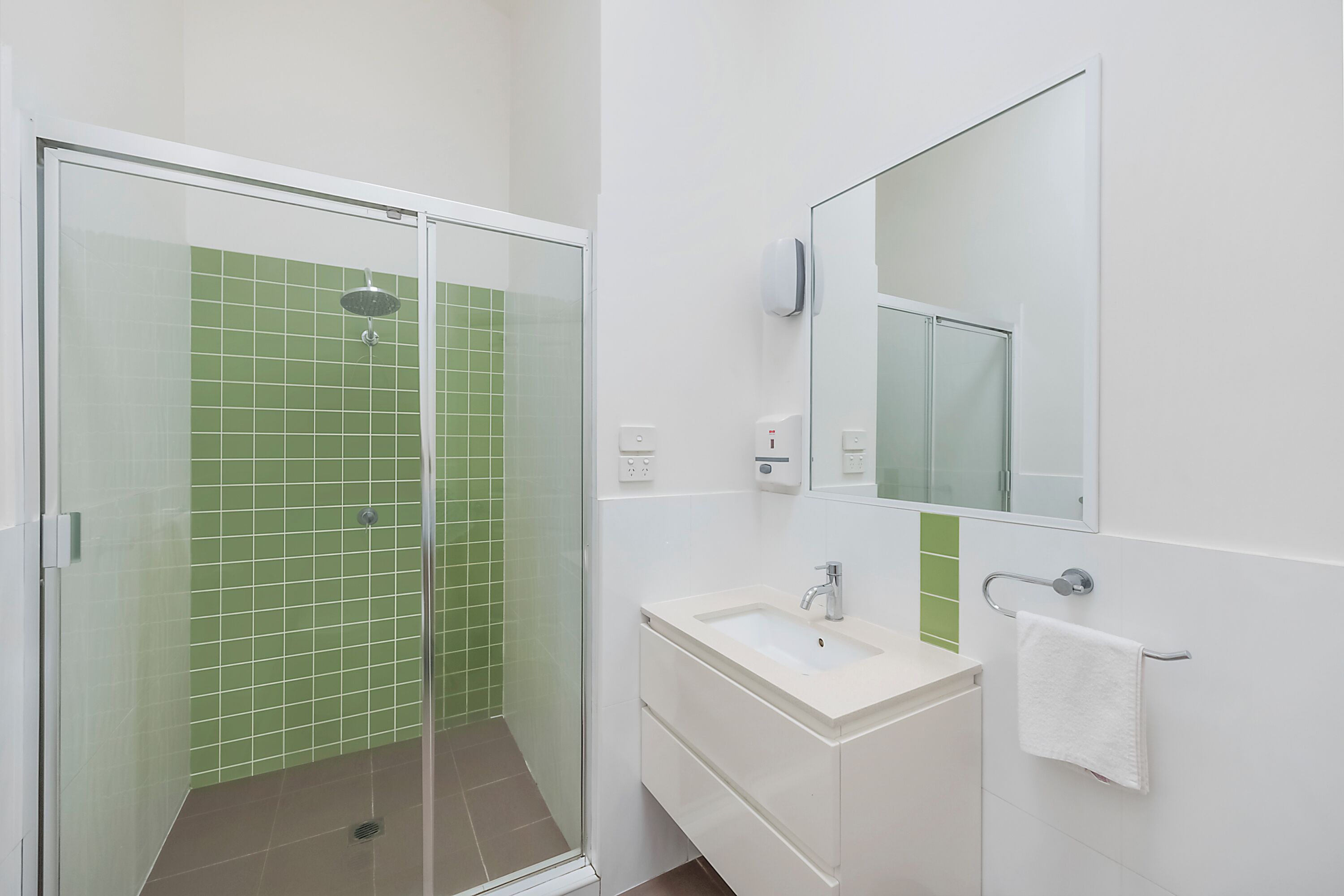 A bathroom with a glass-enclosed shower, a white sink, and a mirror.