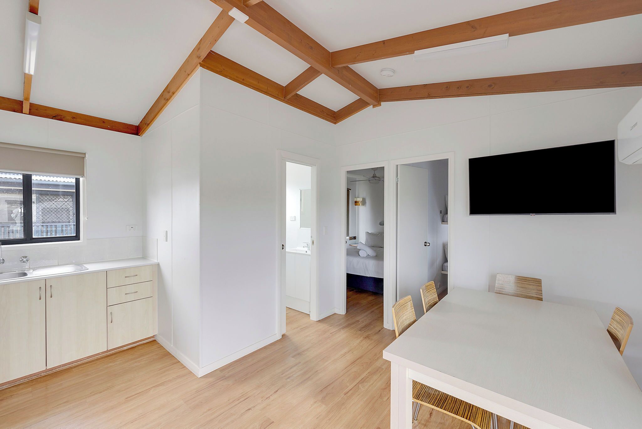 A modern kitchen with wooden beams, a dining area with a table and chairs, and a TV mounted on the wall.