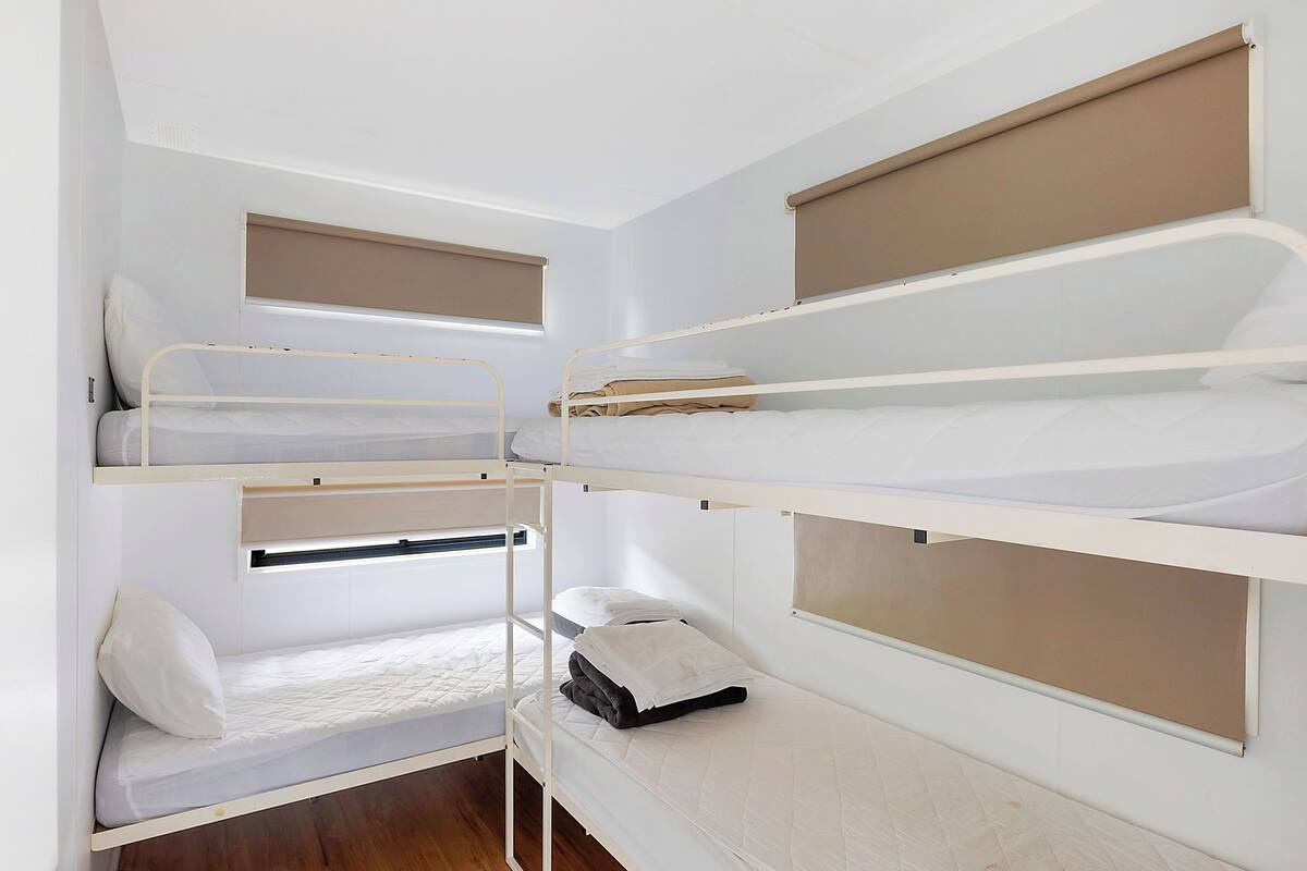A bunk bed room with three levels, each with a mattress and pillows.