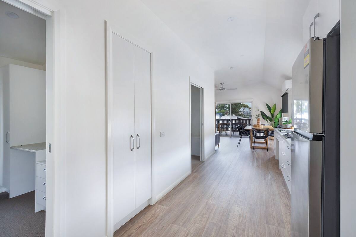 A modern kitchen with a refrigerator, a dining area with a table and chairs, and a hallway with a wardrobe.