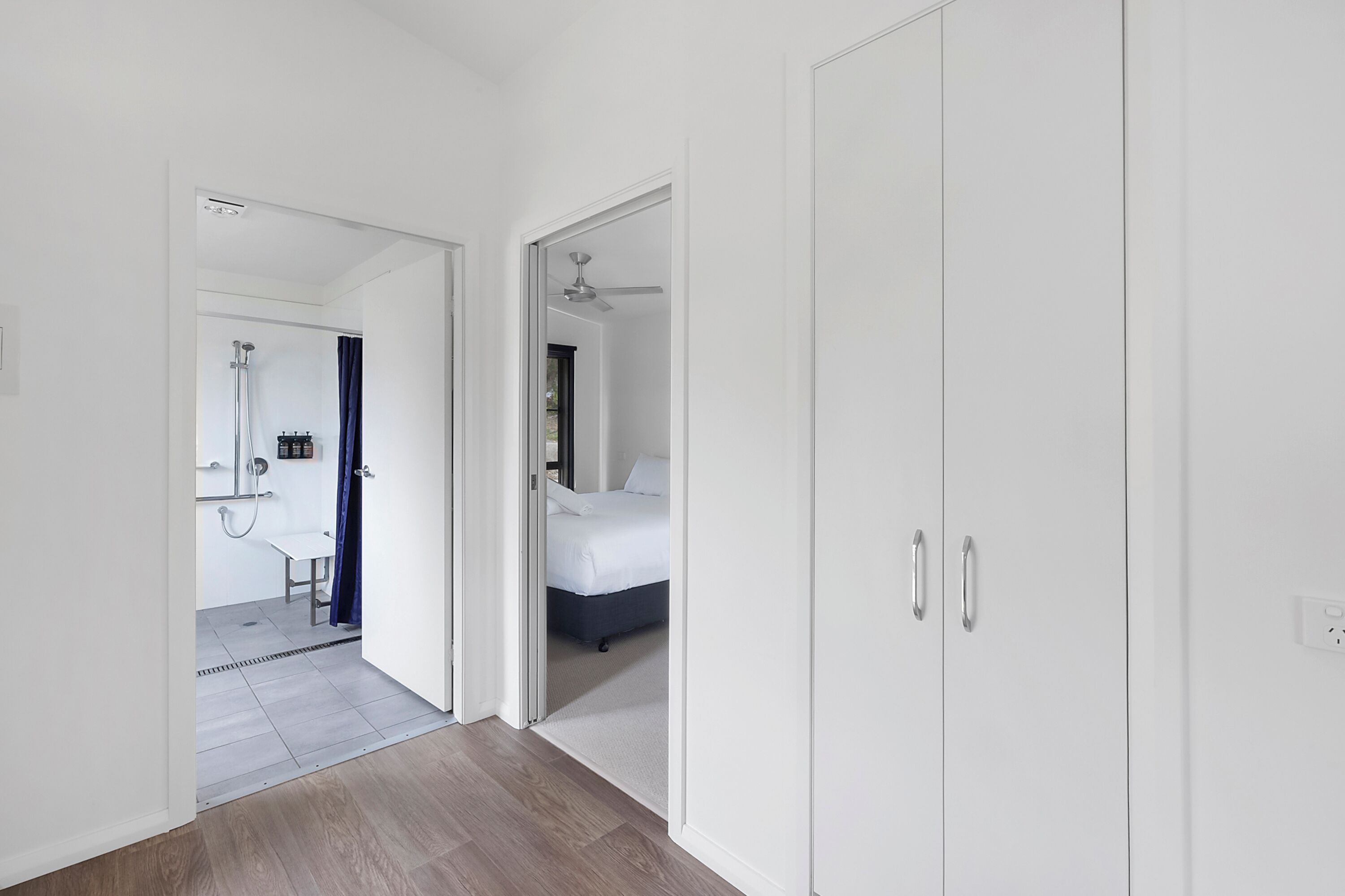 Quarto moderno com cama, guarda-roupa e banheiro visível através de uma porta aberta.