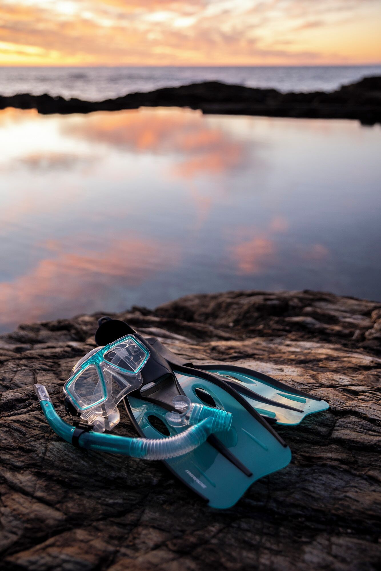 Un equipo de snorkel sobre una superficie rocosa con un atardecer de fondo.