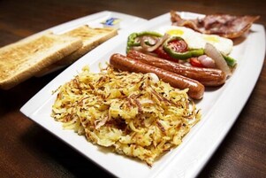 Aamiainen, jossa on paahtoleipää, makkaroita, kananmunia, paprikaa ja perunaraastetta.
