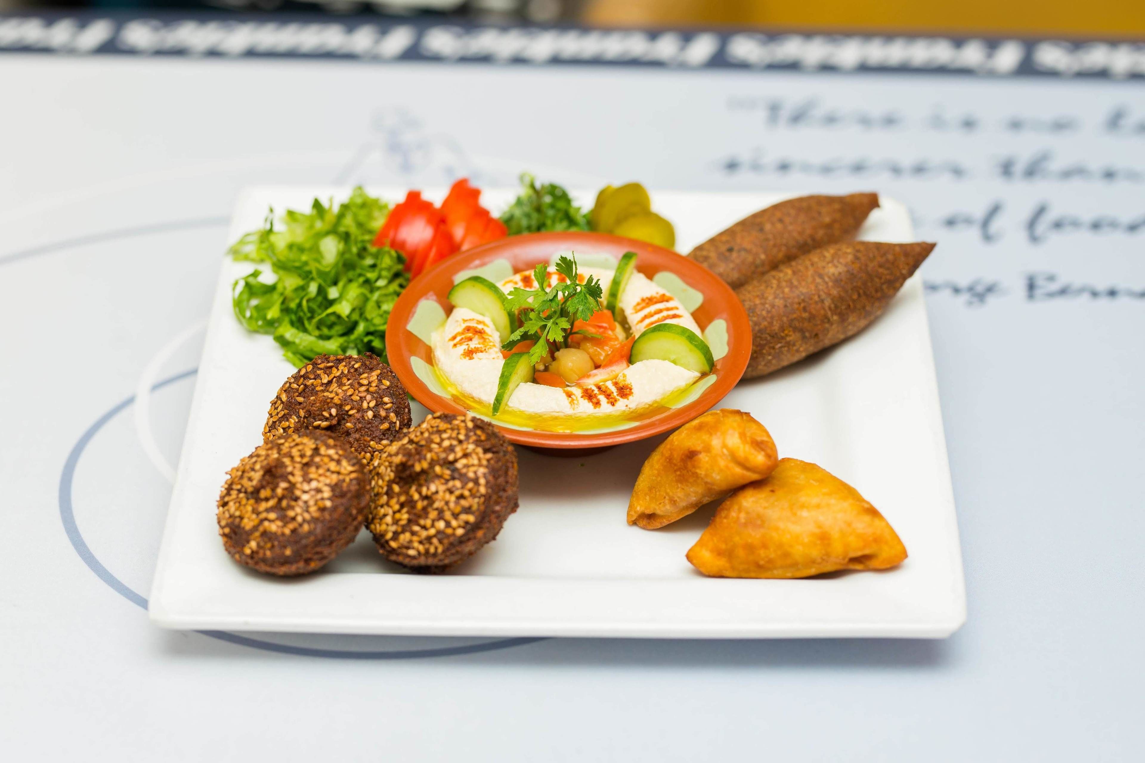 A plate of food including hummus, vegetables, and pastries.
