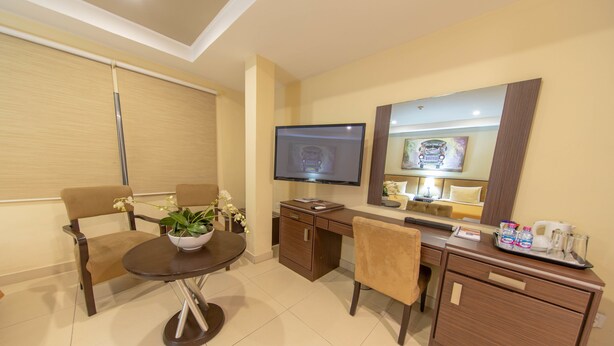 Habitación de hotel con comedor, televisor montado en la pared, escritorio con espejo y bandeja con artículos de tocador.