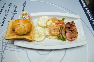 A plate with toast, eggs, onions, peppers, and bacon on a table with a blue tablecloth and a decorative border.