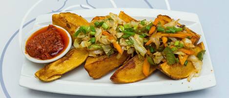 A plate of food with roasted potatoes and vegetables, and a small bowl of sauce.