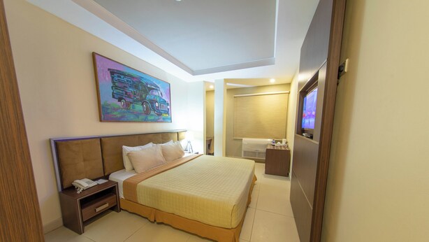 Una habitación de hotel moderna con una cama grande, una mesita de noche con teléfono, un cuadro en la pared y un televisor en la esquina.