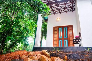 Traditional building with a wooden door and a geometric pattern, set amidst lush greenery and a stone wall.