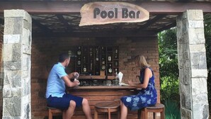 A pool bar with a rustic wooden sign, a brick wall, and a bar stocked with bottles. - Garcinia Leaf (Hikkaduwa)