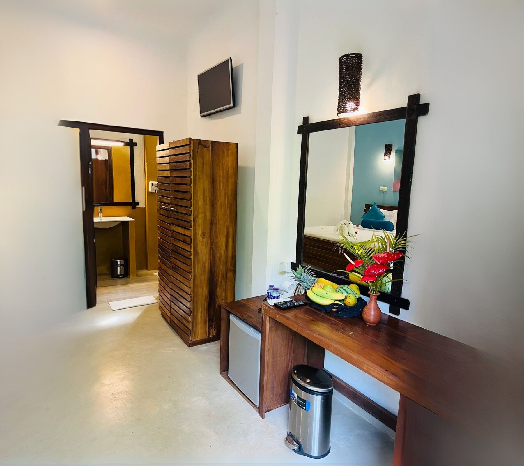 Una habitación de hotel con un armario de madera, un pequeño escritorio con espejo y un cesto de basura.