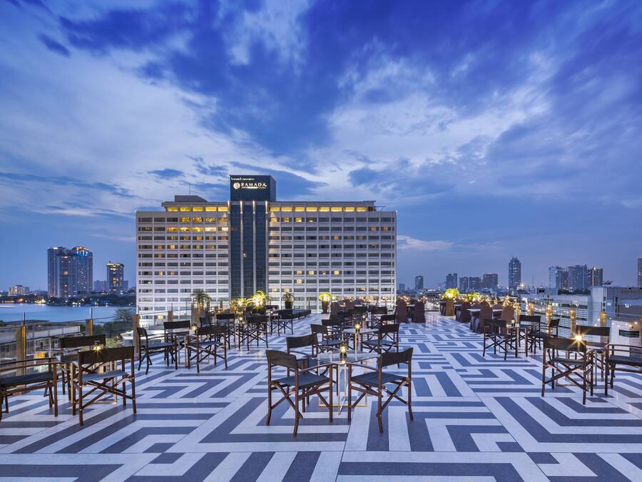 A rooftop terrace with outdoor seating and a view of a city skyline at dusk.