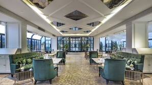 A spacious indoor area with a central seating area featuring green upholstered sofas and tables, large windows providing natural light, and a patterned floor. - Hotel Once Bangkok (Bangkok)