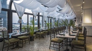 A restaurant with tables set for dining, potted plants, and a city view through large windows. - Hotel Once Bangkok (Bangkok)