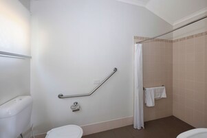 Un baño con inodoro, barra de apoyo, cortina de ducha y toallero.