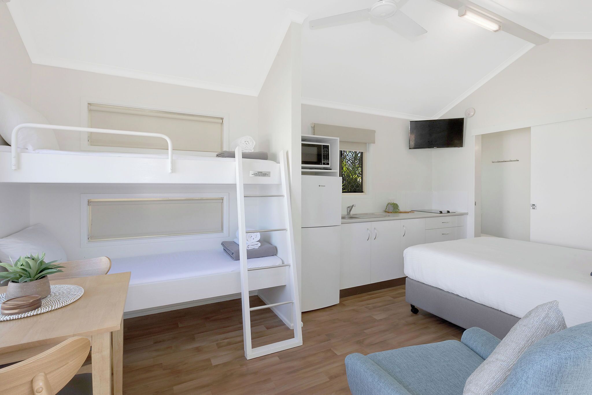A compact, modern room with a bunk bed, a small kitchenette, a sofa, and a dining table.
