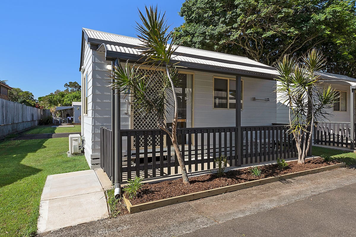 A single-story mobile home with a fenced yard, a small garden, and a clear sky.