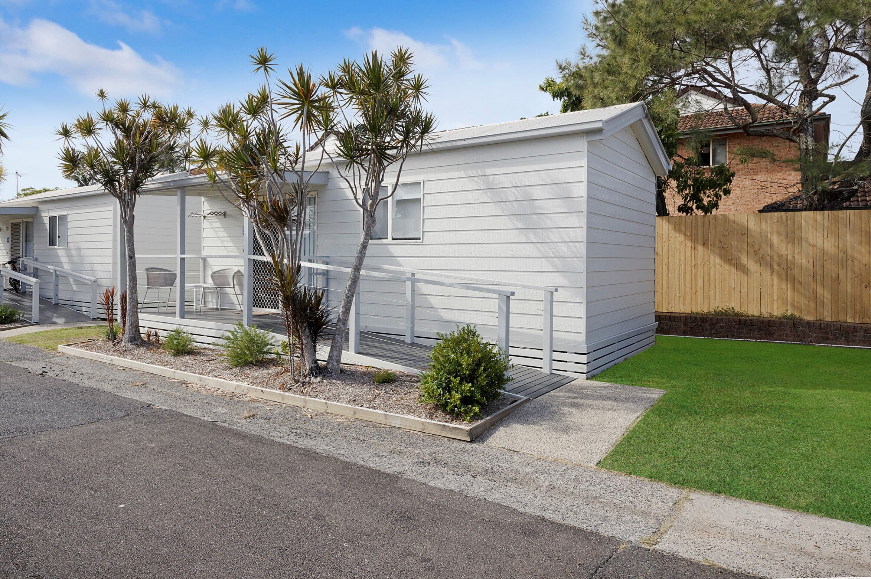 A single-story mobile home with a small patio area, a covered outdoor seating area, and a fenced yard.