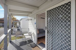 A covered outdoor area with a white railing, a wicker chair, a small table, and a grey sofa inside a house. - Reflections Ballina - Holiday Park (Ballina)