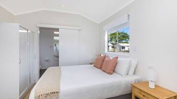 Un dormitorio con cama, mesita de noche y ventana.